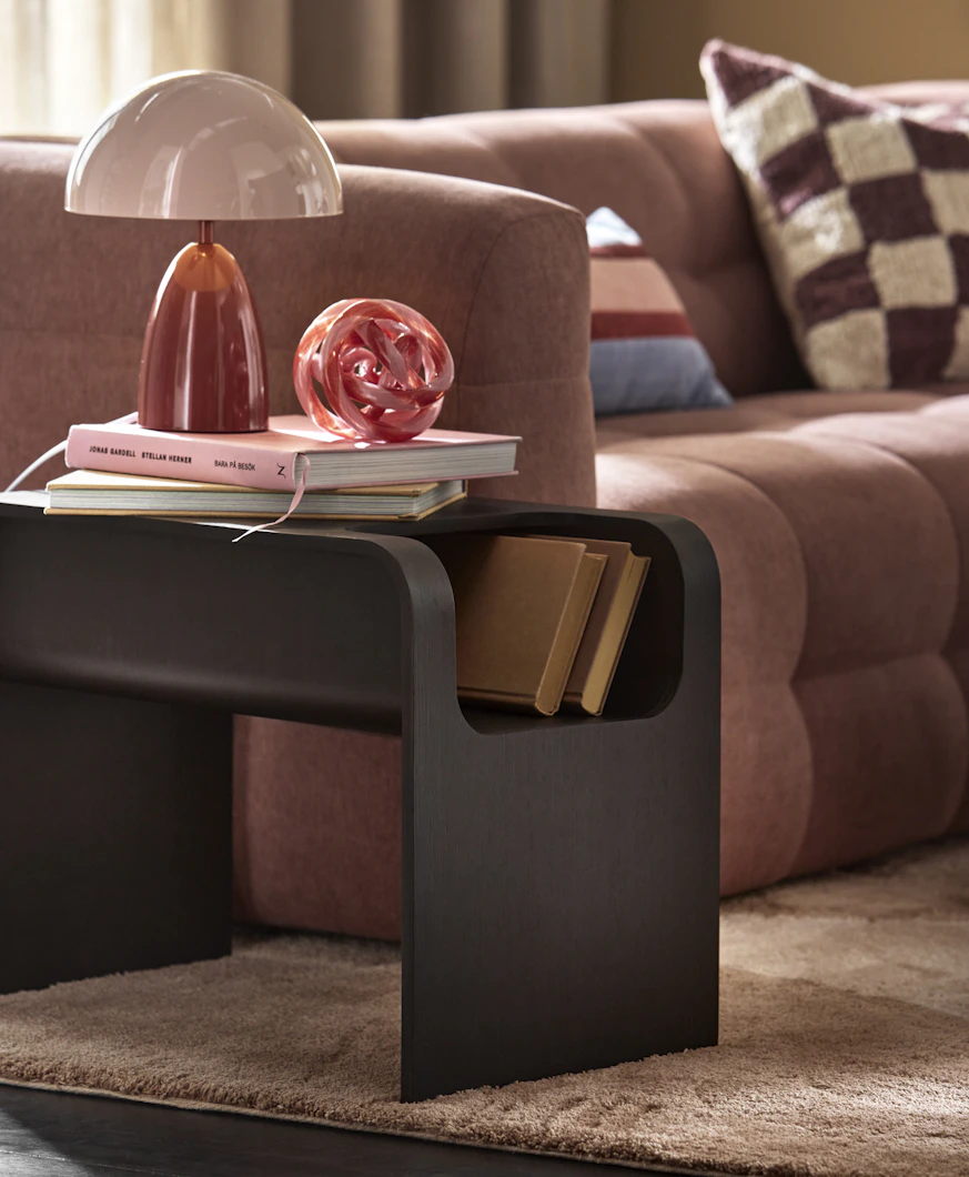 Bredvid en rosa soffa står ett sidobord i mörkt trä
