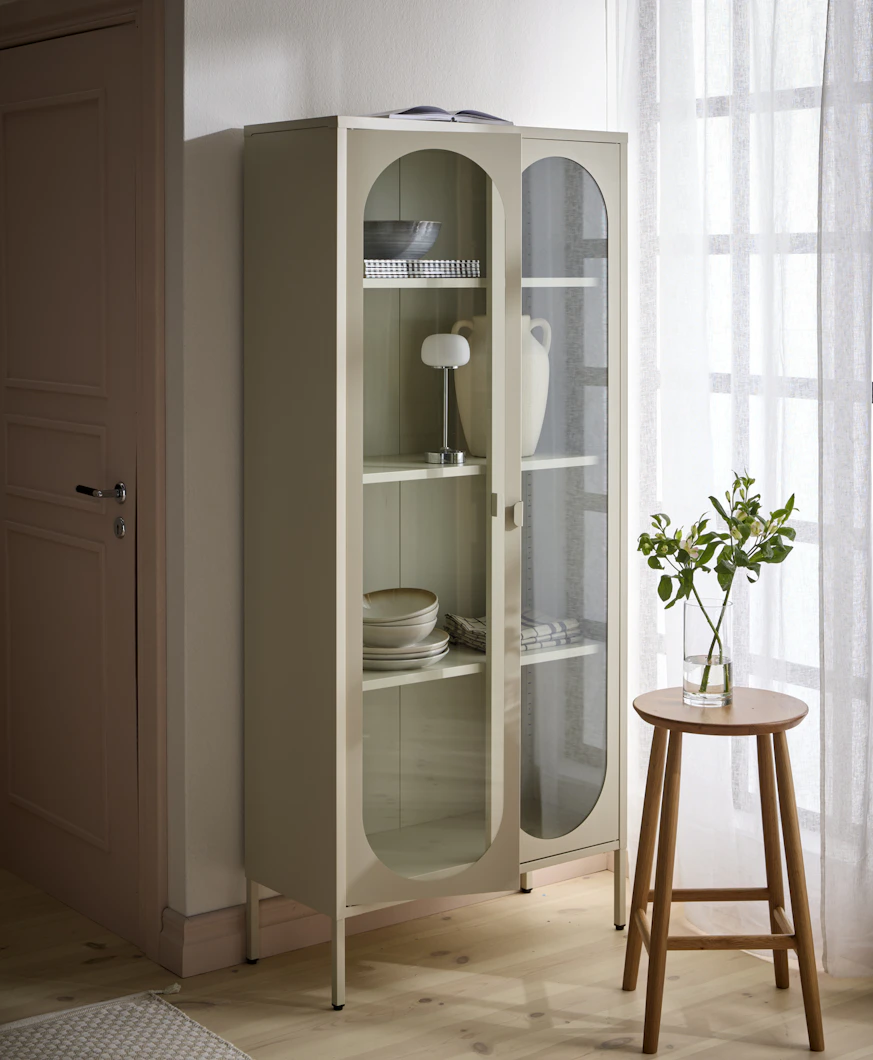 Ett beige vitrinskåp är fyllt med porslin, en urna och en lampa.