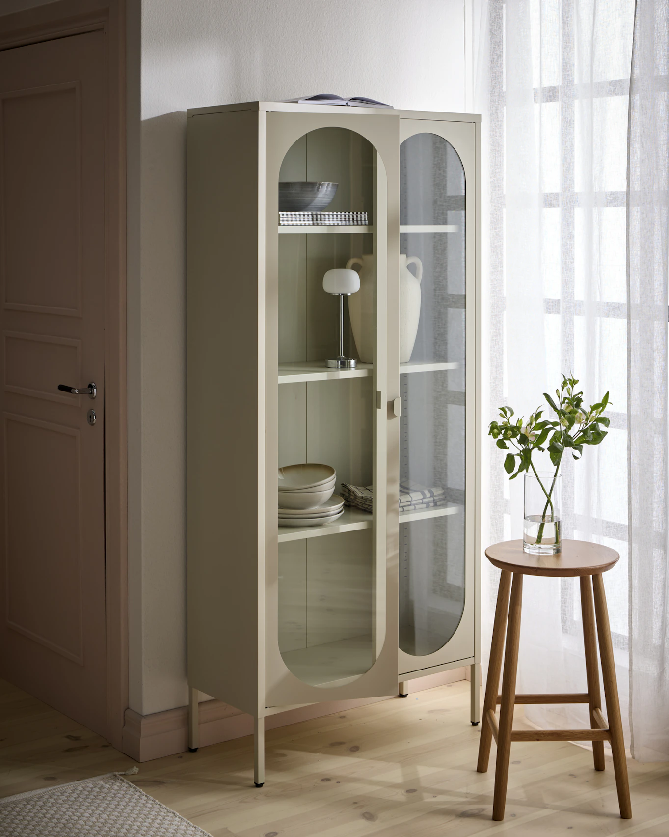 Ett beige vitrinskåp är fyllt med porslin, en urna och en lampa.