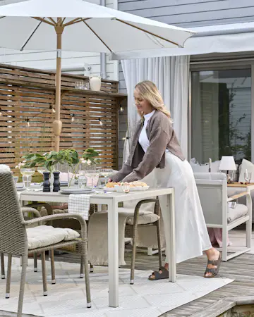Ung kvinna i vit klänning och brun dukar upp porslin på ett bord på en uteplats