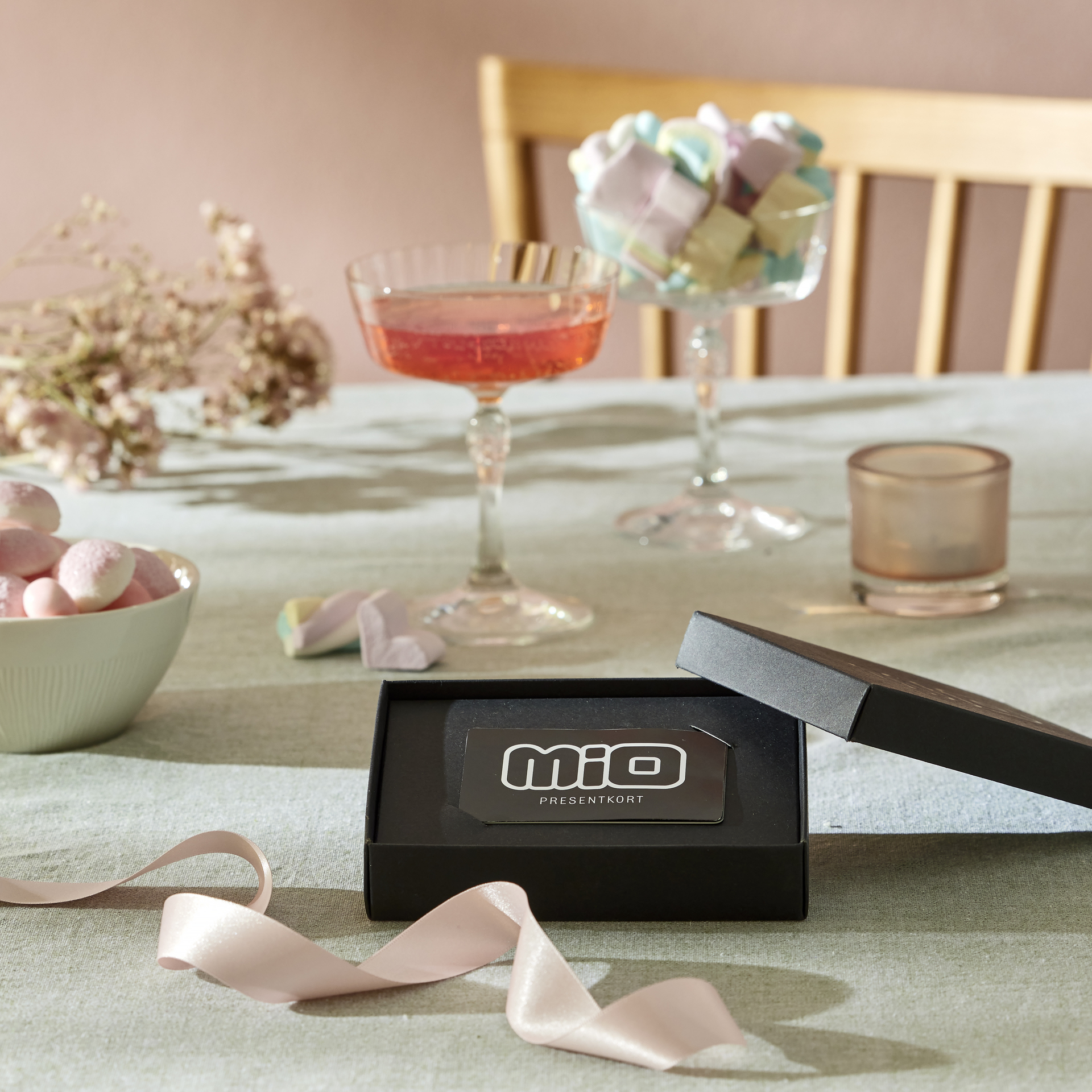 ett presentkort i en svart ask ligger på ett bord där det även står glas, godis, och en ljuslykta