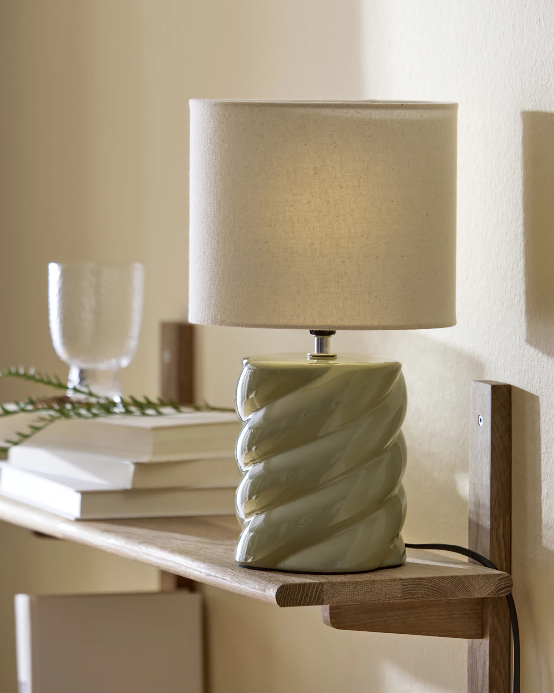 Bordslampa med lampskärm i ljus beige och lampfot i ljusgrönt med skruvad form.