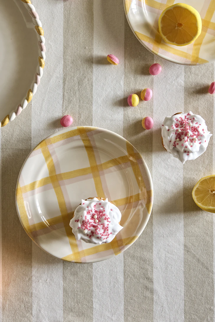 Tallrik med rutat gult mönster står på bord med beige/vit randig duk.