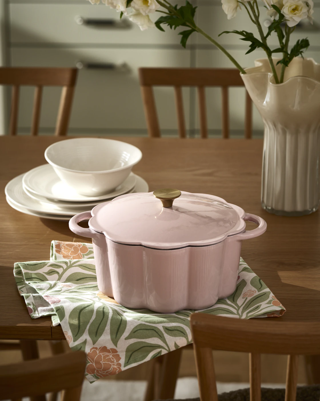 Rosa gryta i form av en blomma står på på ett mörk matbord.