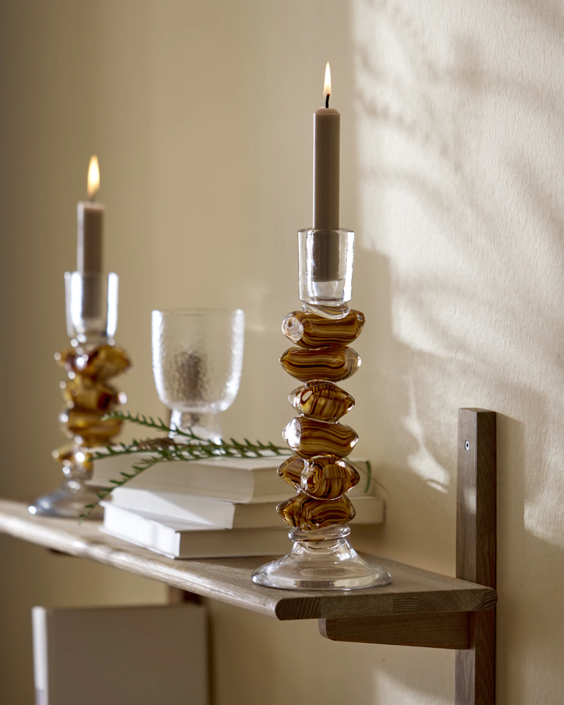 Ljusstake med fot i form av bruna karameller står på en vägghylla i trä.