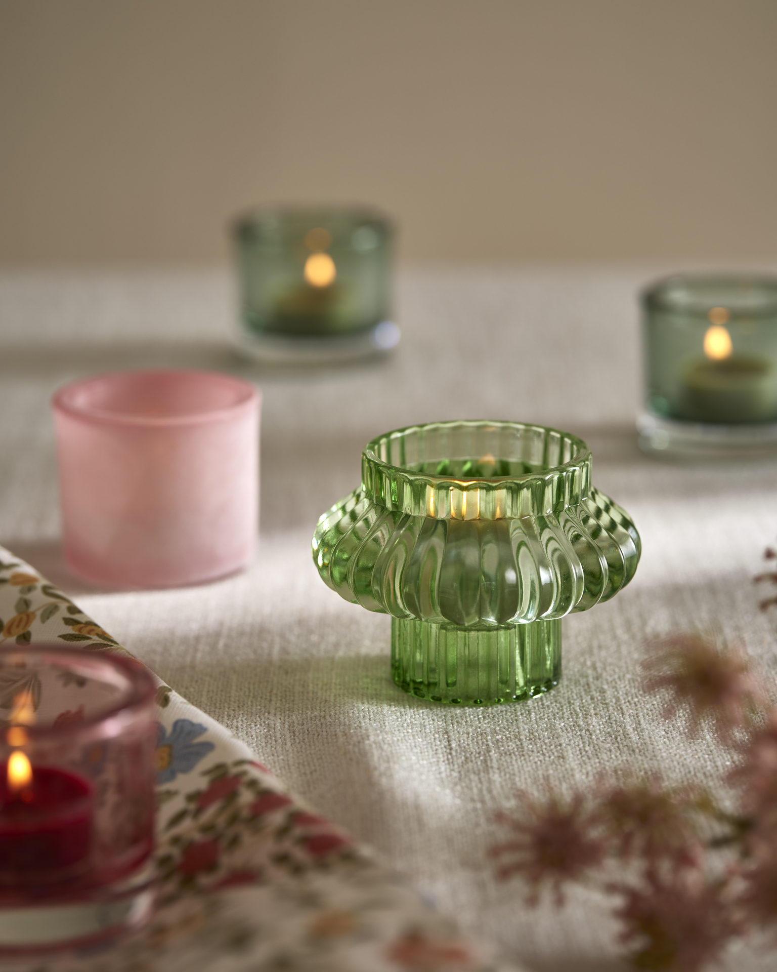 Tre gröna och en rosa ljuslykta i olika modeller står på en duk.