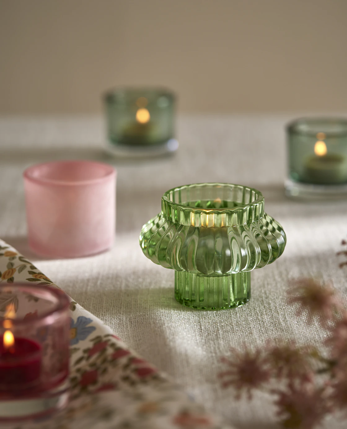 Tre gröna och en rosa ljuslykta i olika modeller står på en duk.