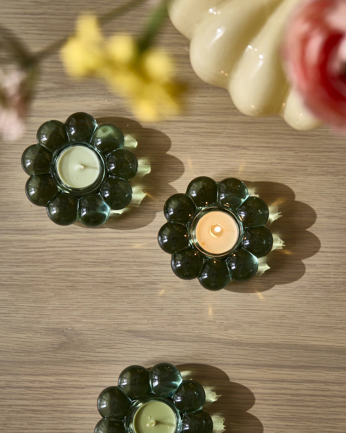 Tre gröna ljuslykor i form av en blomma står på ett bord.