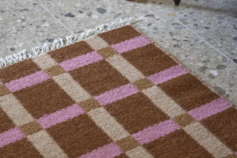 På en beige matta med ett strukturerat mönster står en fåtölj i zebramönster ich en pall i mörkt trä