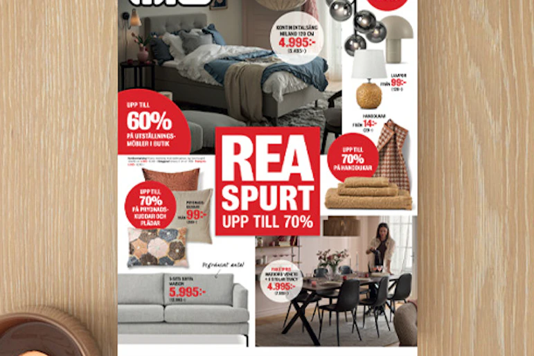 Ett kampanjblad för rea ligger på ett ljust träbord med en blomma och ljuslykta bredvid