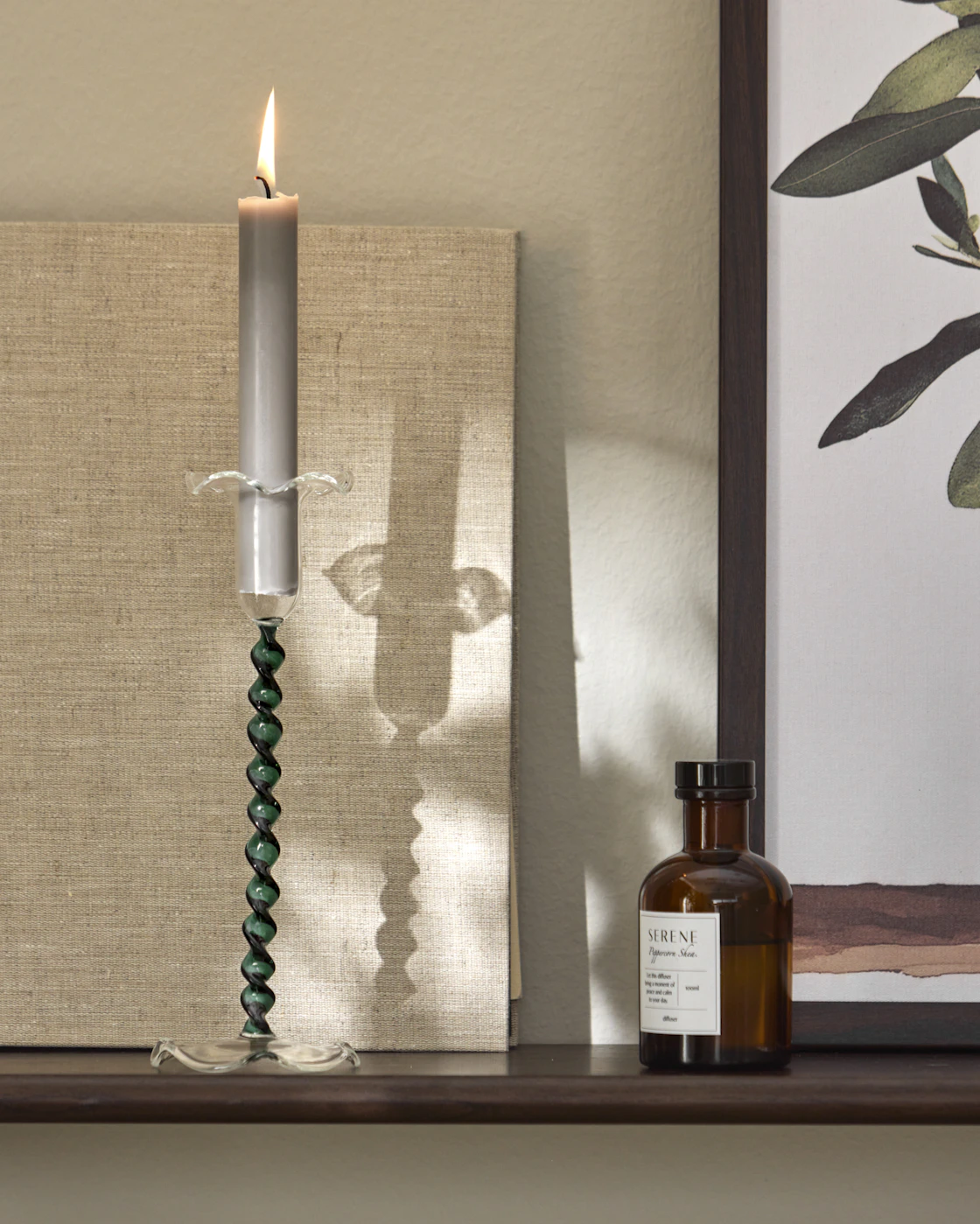 En swirlad grön ljusstake med ett grått ljus står på en hylla.