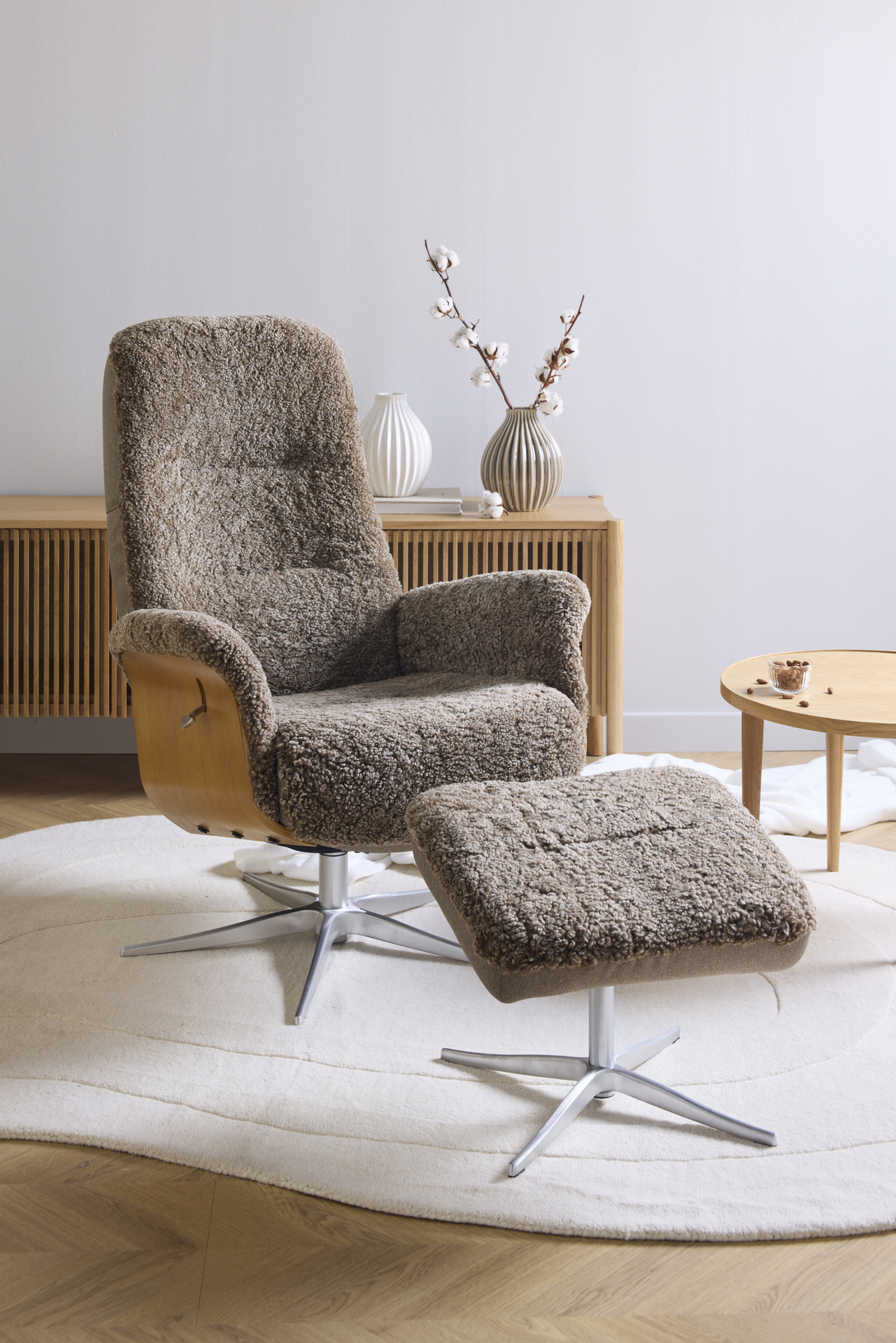 Framför en tv-bänk i ljust trä står en brun fårskinnsfåtölj med underrede i ek