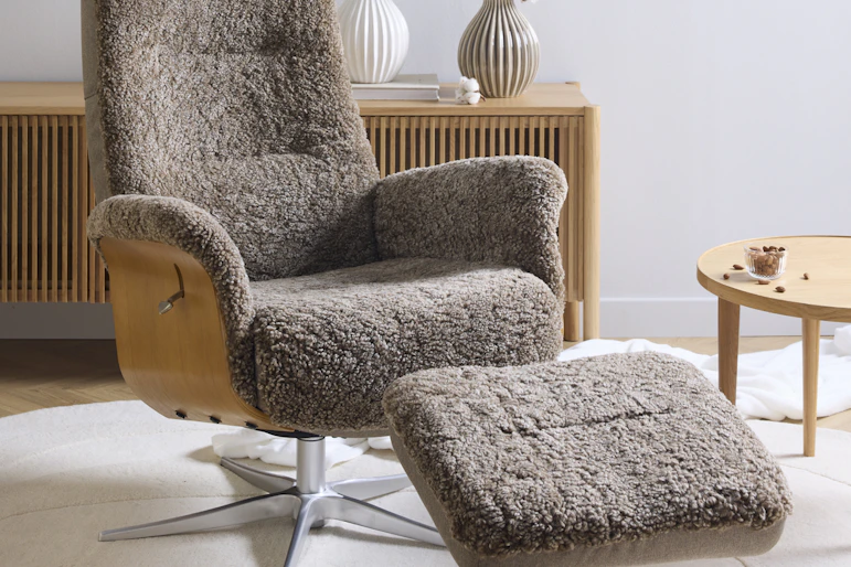 Framför en tv-bänk i ljust trä står en brun fårskinnsfåtölj med underrede i ek