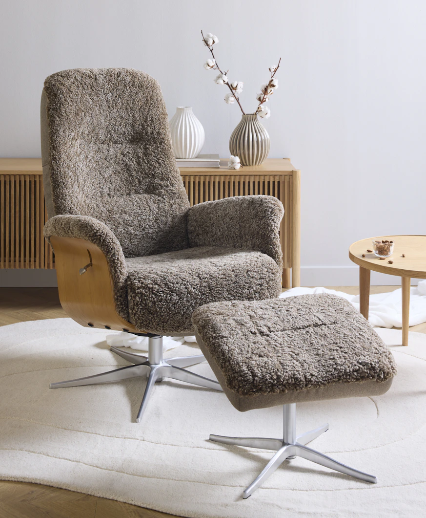 Framför en tv-bänk i ljust trä står en brun fårskinnsfåtölj med underrede i ek