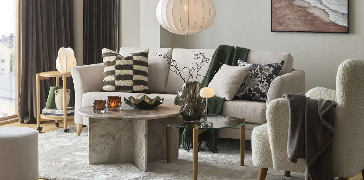 I ett avskalat vardagsrum står en beige soffa bakom ett soffbord i marmor