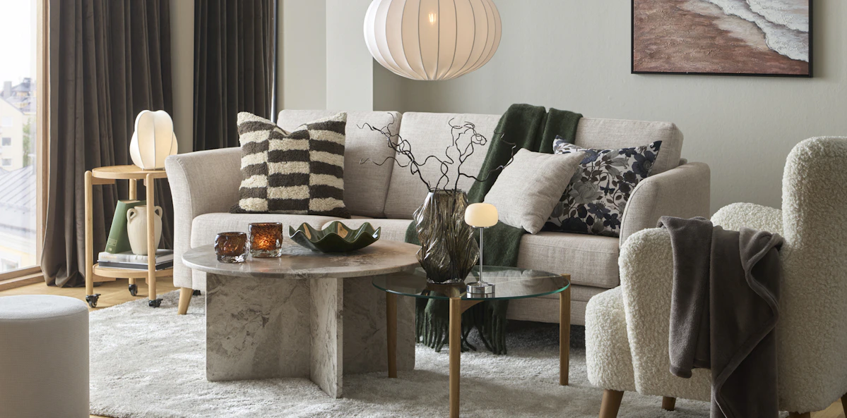 I ett avskalat vardagsrum står en beige soffa bakom ett soffbord i marmor