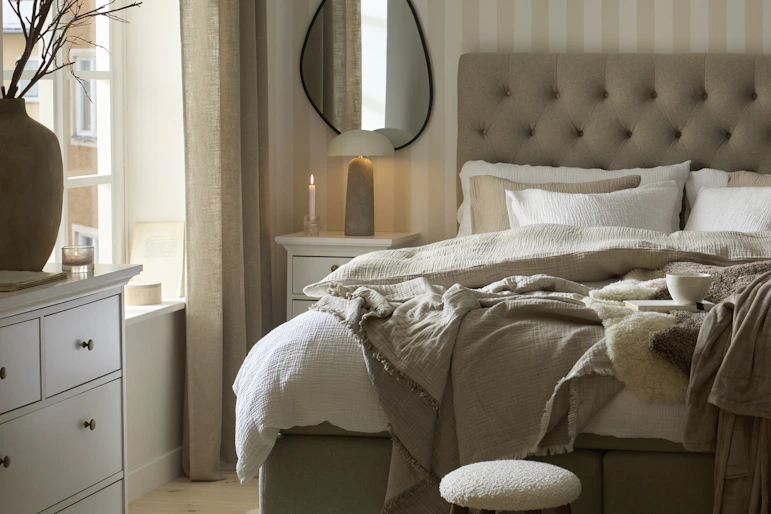 en grå kontinentalsäng står i ett ljust sovrum