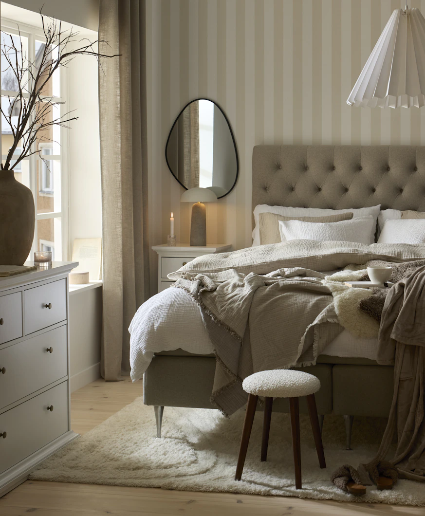 en grå kontinentalsäng står i ett ljust sovrum