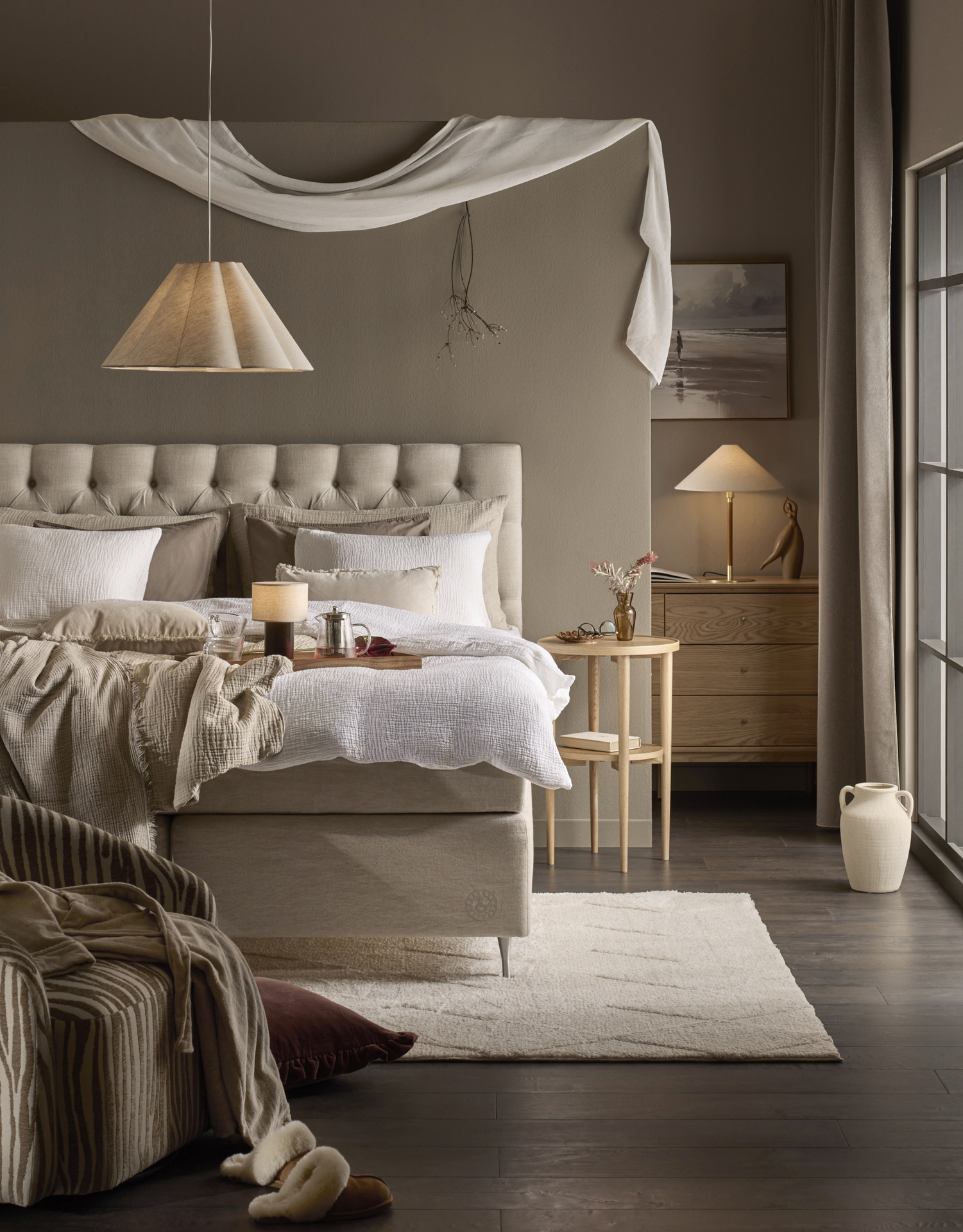 en beige kontinentalsäng med pikerad gavel står i ett beiget sovrum med vita lakan