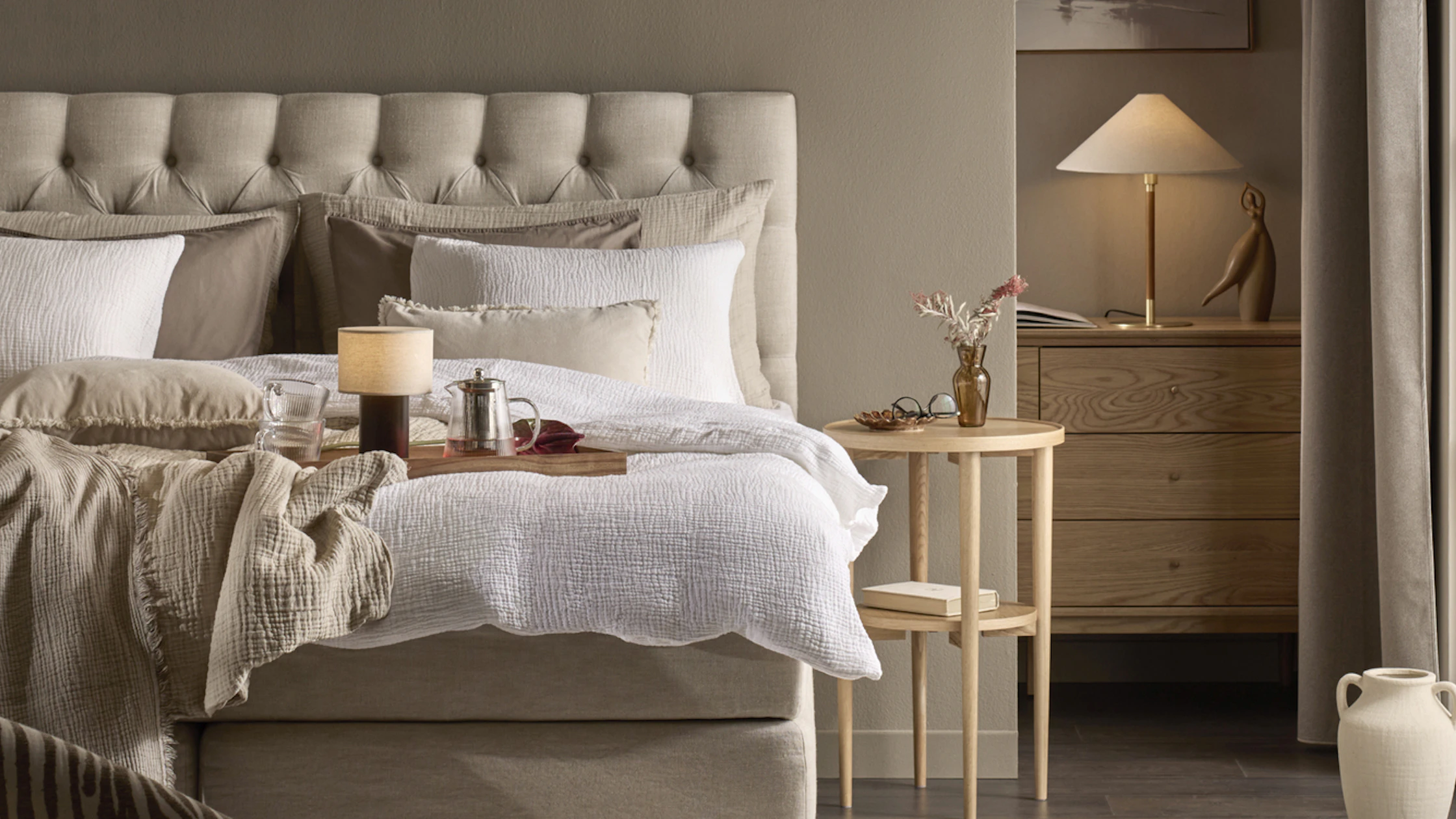 en beige kontinentalsäng med pikerad gavel står i ett beiget sovrum med vita lakan