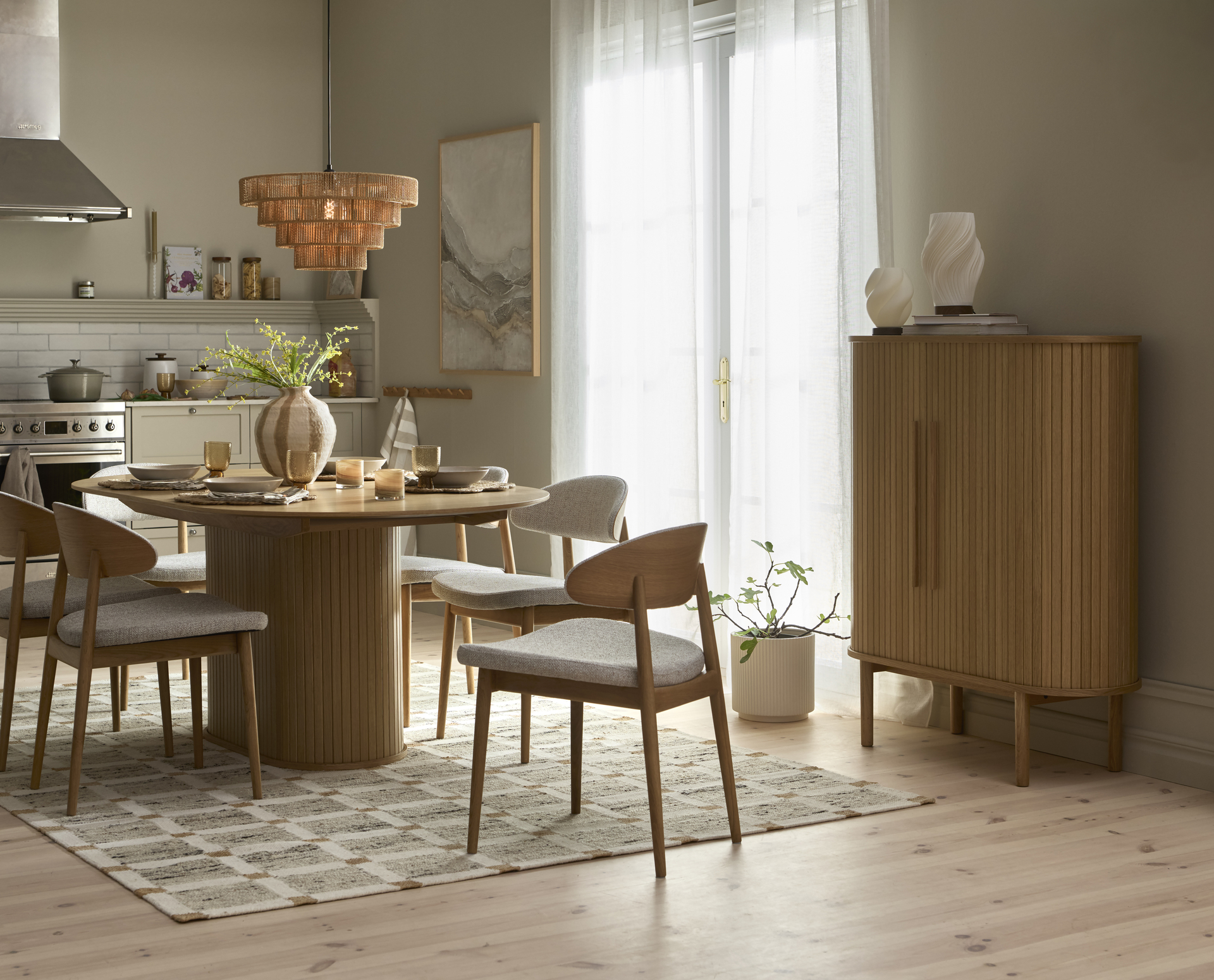 ett rektangulärt matbord med rundade kanter står på en rutig matta i ett kök med fyra stolar runt sig