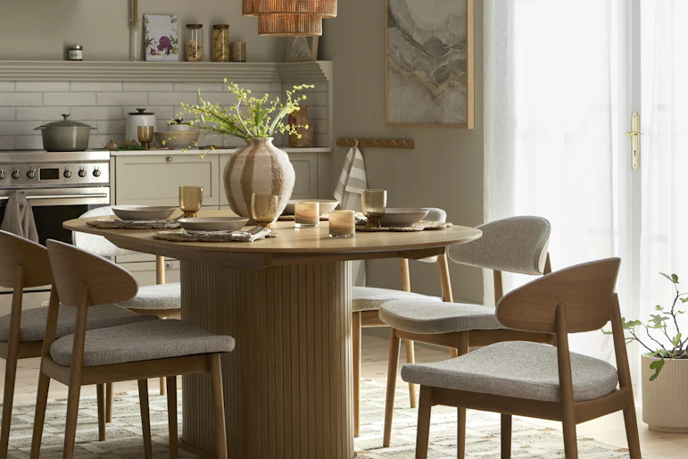 ett rektangulärt matbord med rundade kanter står på en rutig matta i ett kök med fyra stolar runt sig