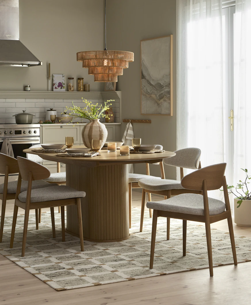 ett rektangulärt matbord med rundade kanter står på en rutig matta i ett kök med fyra stolar runt sig