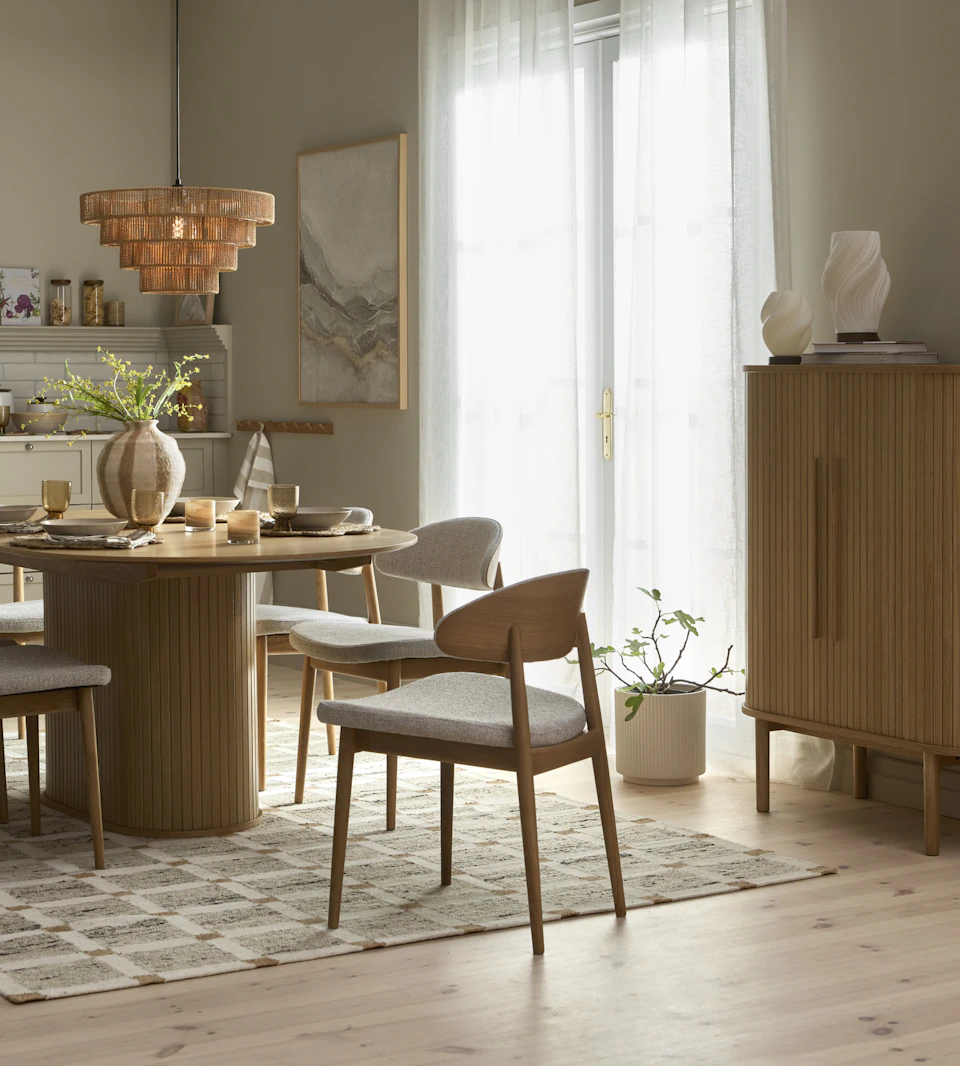 ett rektangulärt matbord med rundade kanter står på en rutig matta i ett kök med fyra stolar runt sig