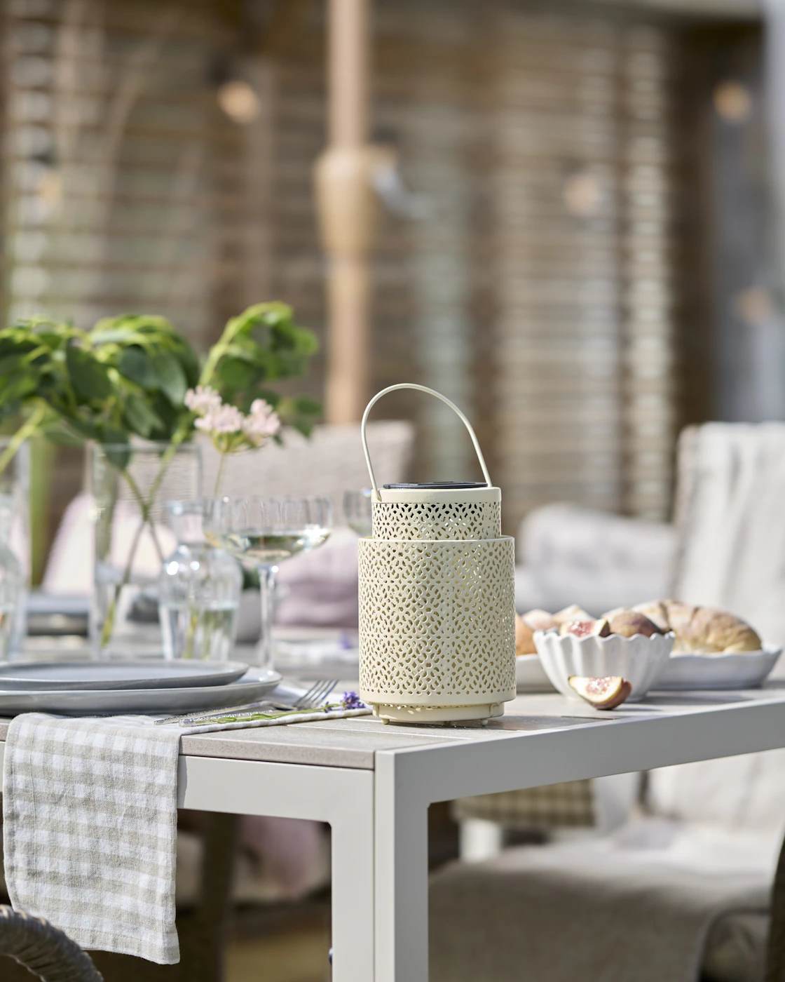 En vaniljfärgad solcellslykta står på ett vitt utebord.