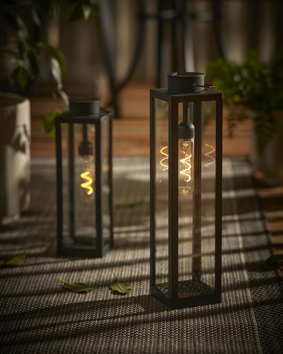 Två svarta solcellslyktor står på en utematta.