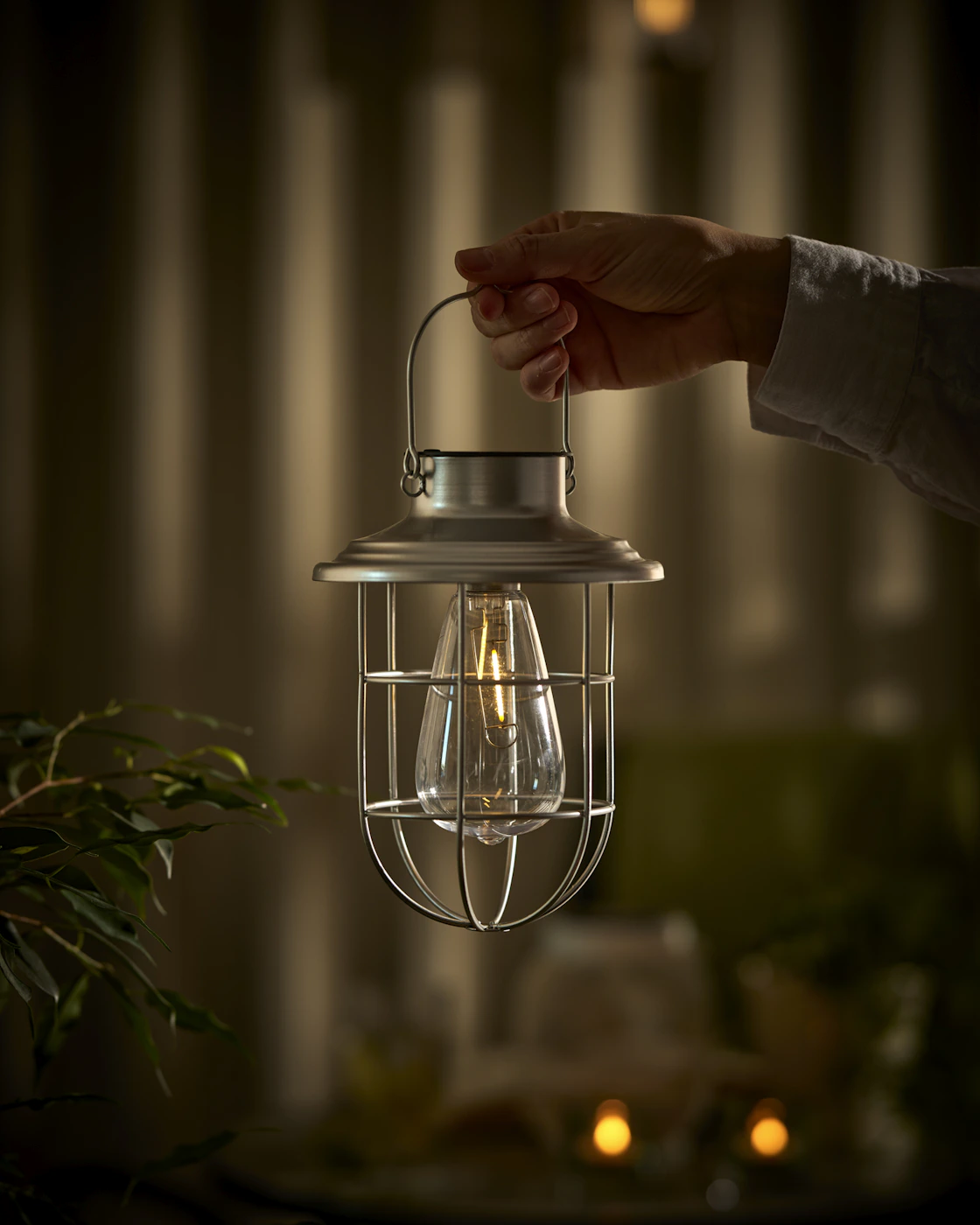 En hand håller i en solcellslykta i rostfritt stål.