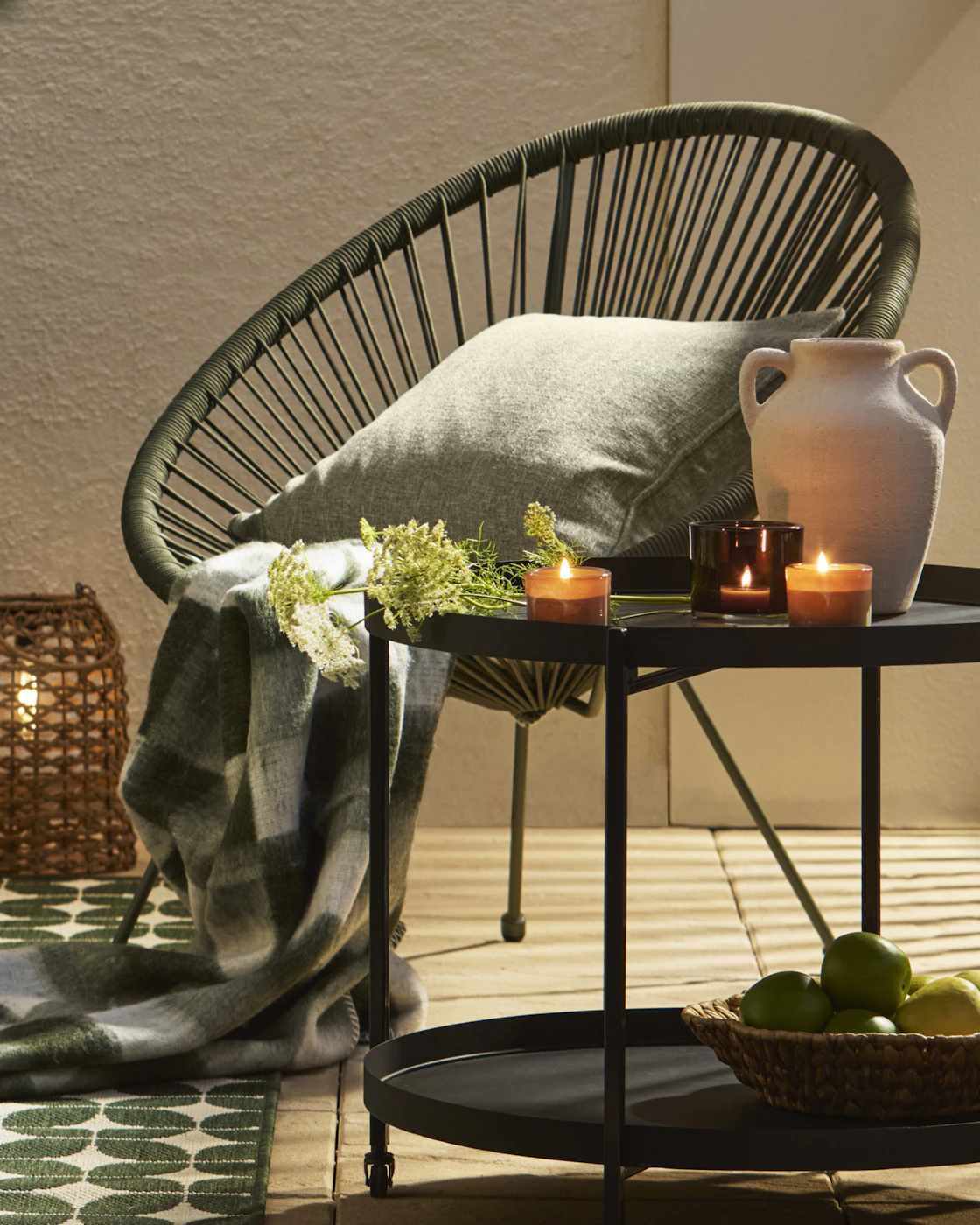 En mörkgrön utefåtölj av polyesterrep står intill ett svart sidobord med tända ljuslyktor.