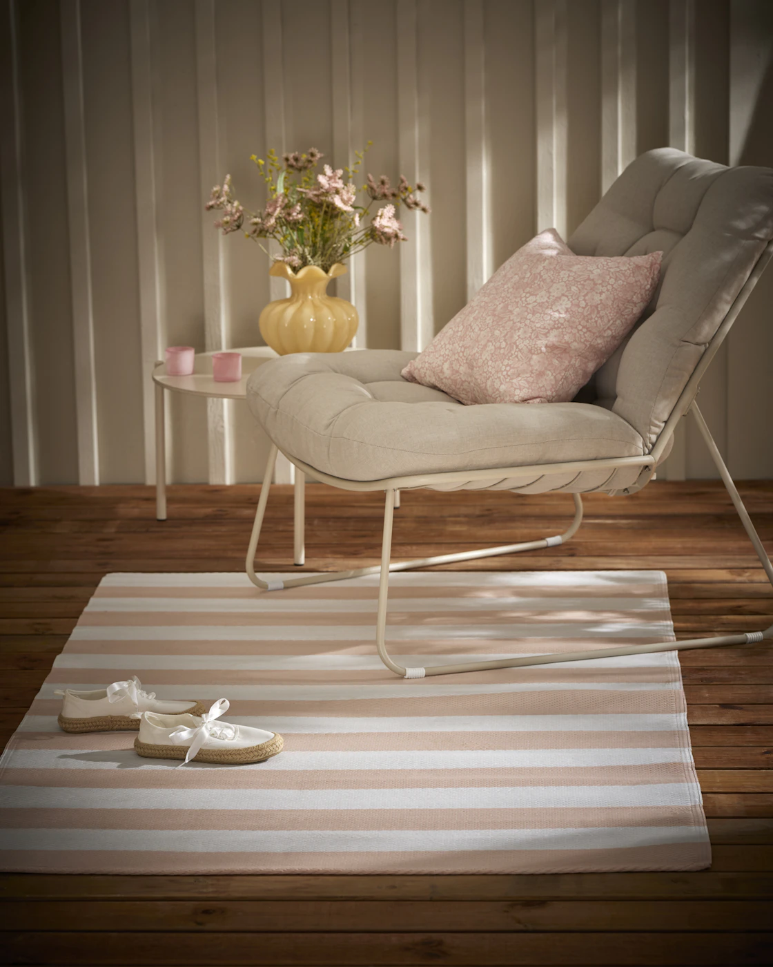 En randig utematta i vitt och rosa ligger under en beige utefåtölj.