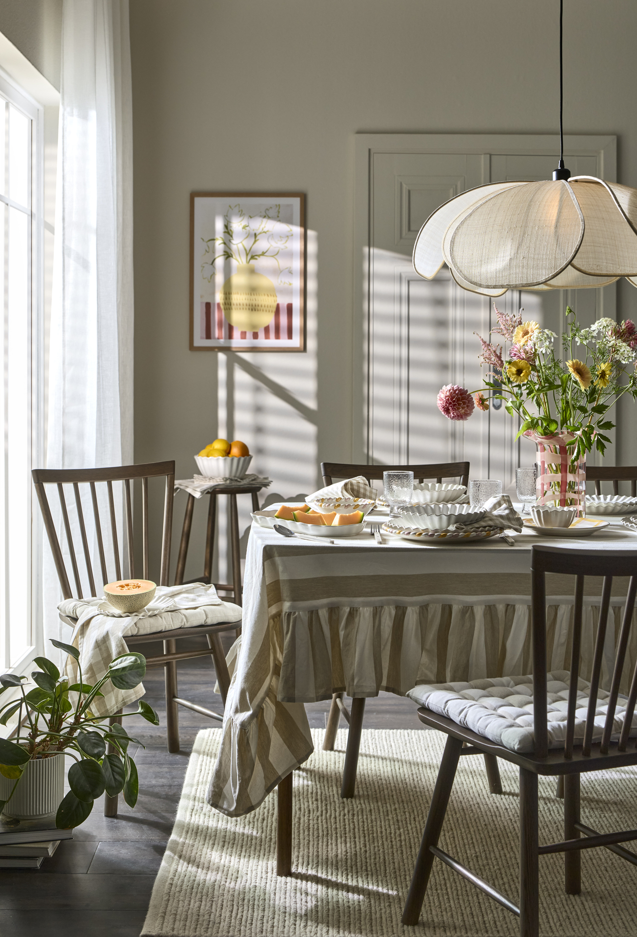   ett bprd med en randig duk är dukat med vitt porslin och en stor rosa vas med blommor