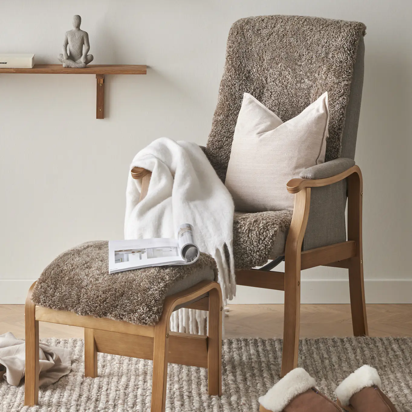 I en brun fårskinnsfåtölj ligger en beige kudde och en vit filt