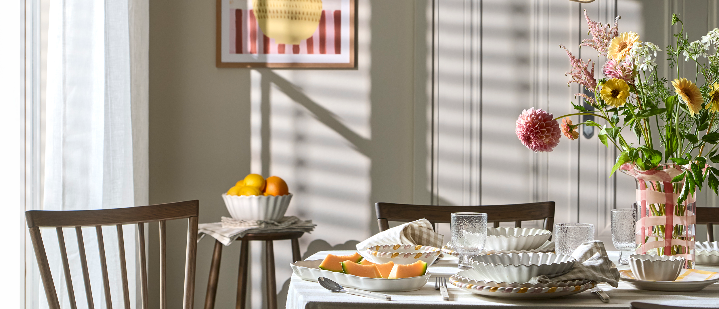 ett bord med en randig duk är dukat med vitt porslin, mat, och en rosa vas med blommor i