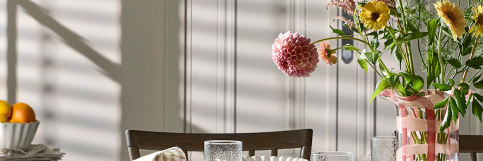 ett bord med en randig duk är dukat med vitt porslin, mat, och en rosa vas med blommor i