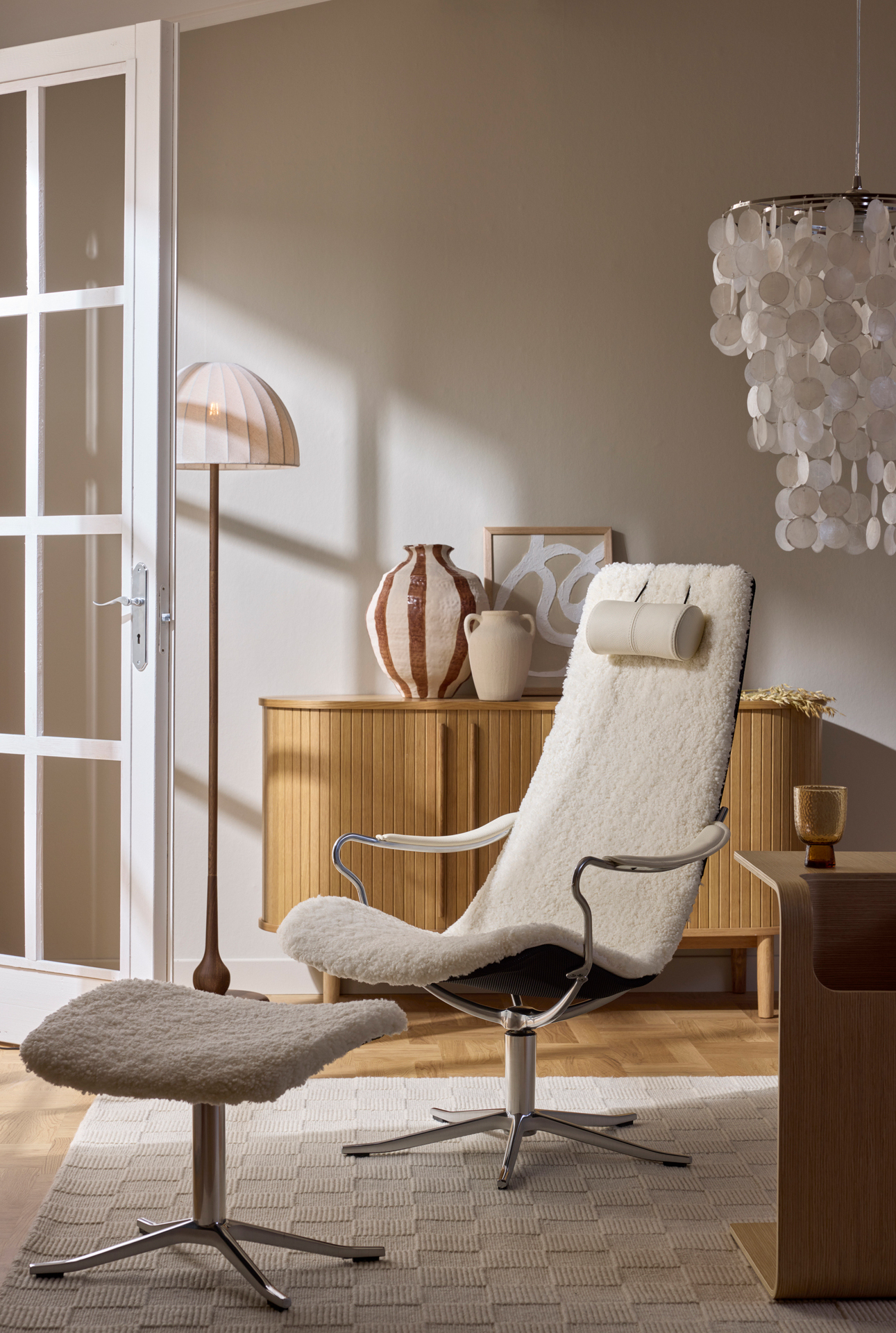 I ett beiget rum står en vit fåtölj i fårskinn framför en ekfärgad skänk