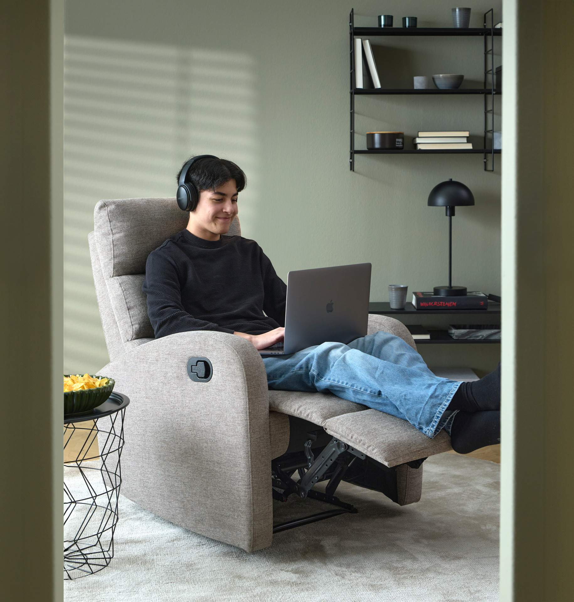 I en grå reclinerfåtölj sitter en ung kille med en laptop i knät