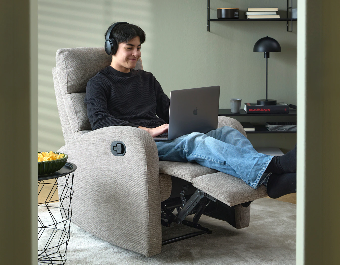 I en grå reclinerfåtölj sitter en ung kille med en laptop i knät