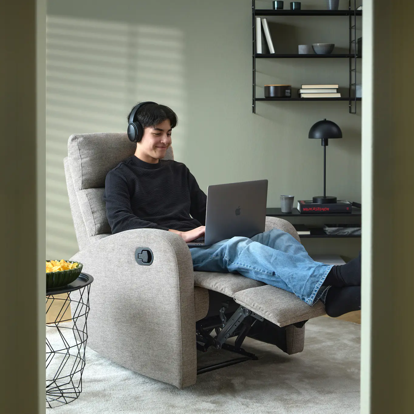 I en grå reclinerfåtölj sitter en ung kille med en laptop i knät