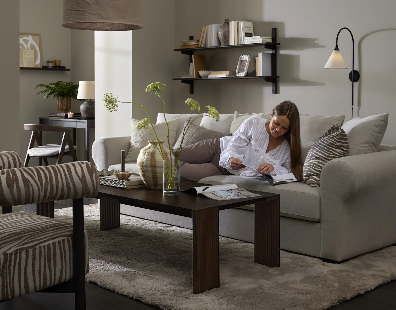 I ett stilrent vardagsrum ligger en kvinna och läser i en vit soffa