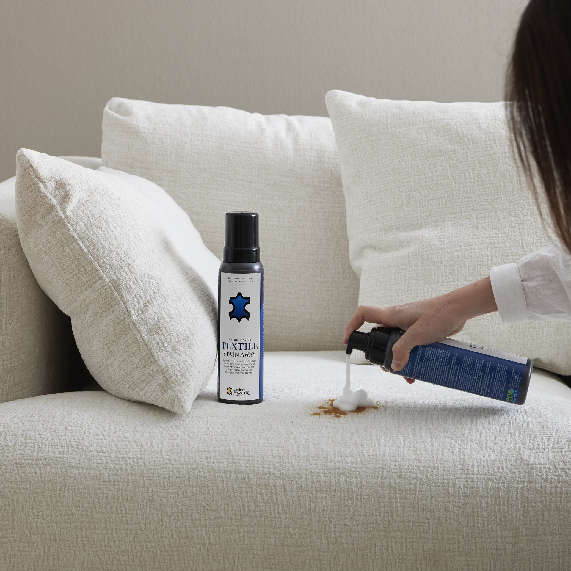 En kvinna sprayar på en fläck i en vit soffa