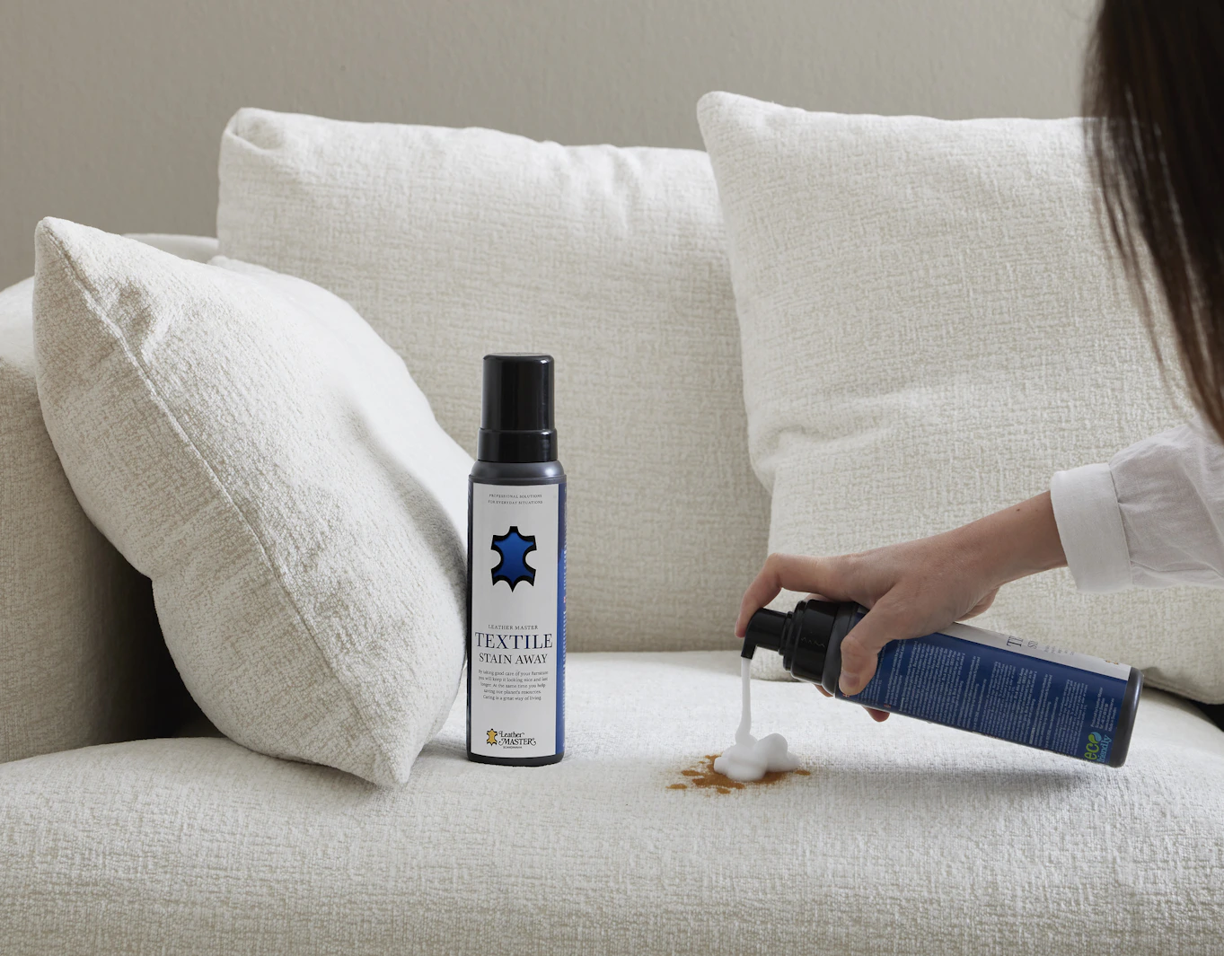 En kvinna sprayar på en fläck i en vit soffa