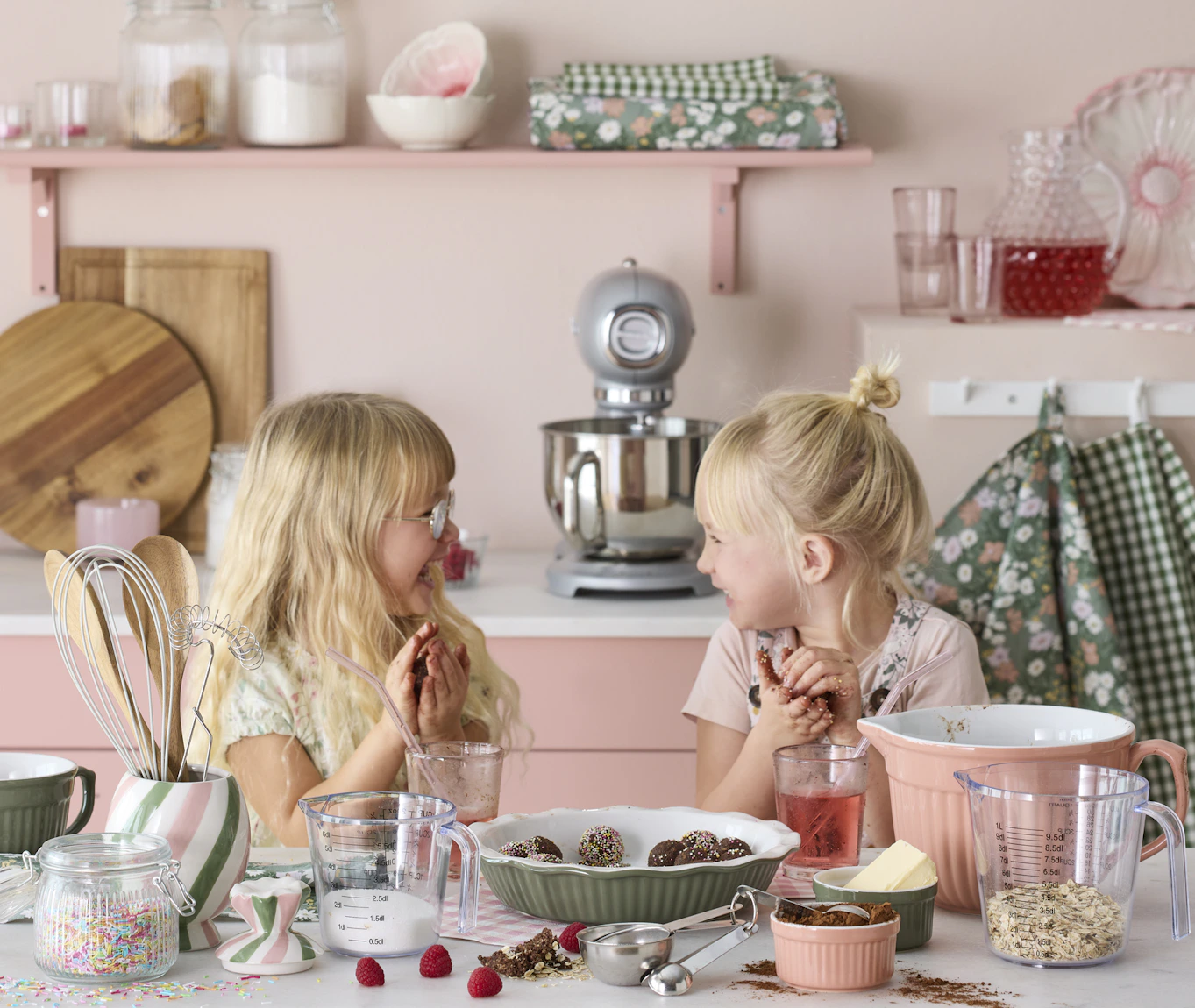 två blonda barn står i ett rosa kök och bakar chokladbollar tillsammans och skrattar