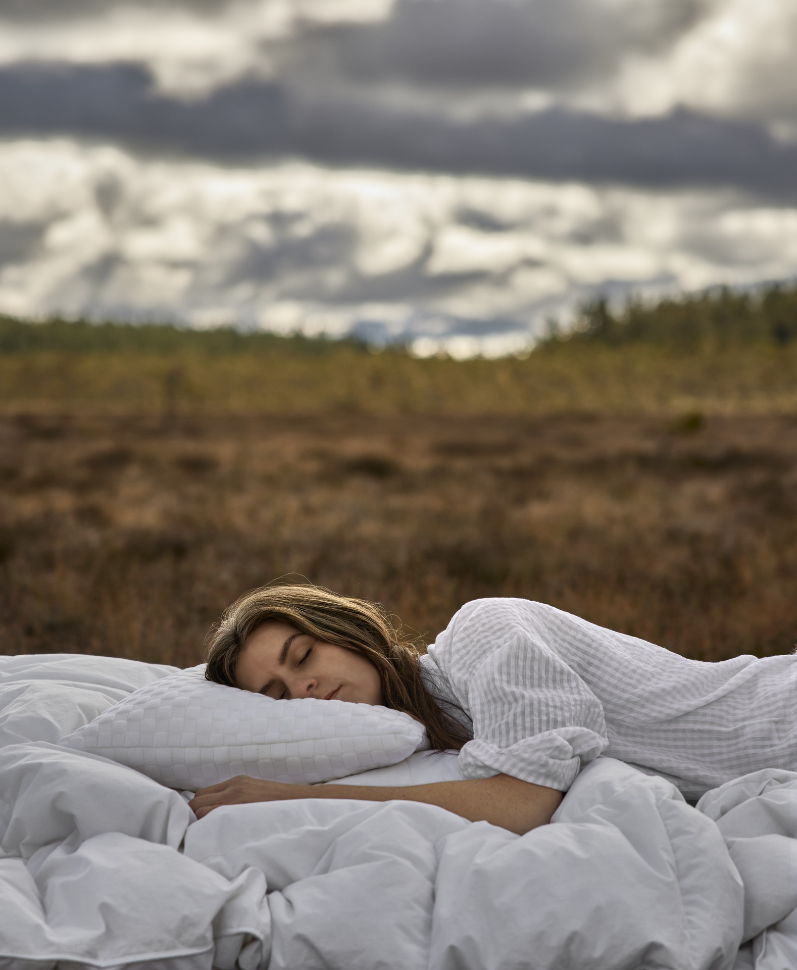 en tjej sover i en säng med vita täcken ute på en äng