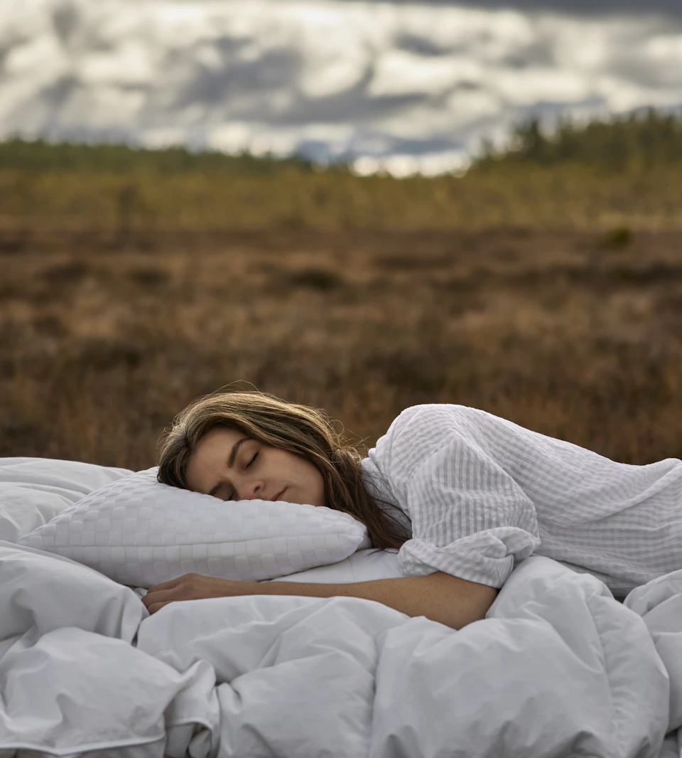 en tjej sover i en säng med vita täcken ute på en äng