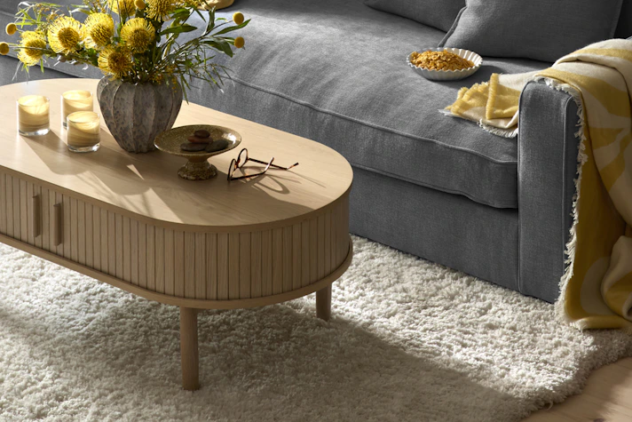 Framför en blå soffa står ett soffbord i vitbetsat trä