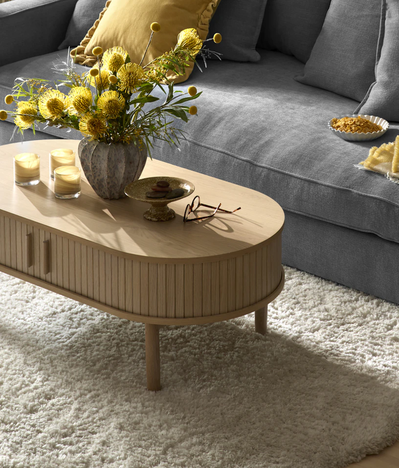 Framför en blå soffa står ett soffbord i vitbetsat trä