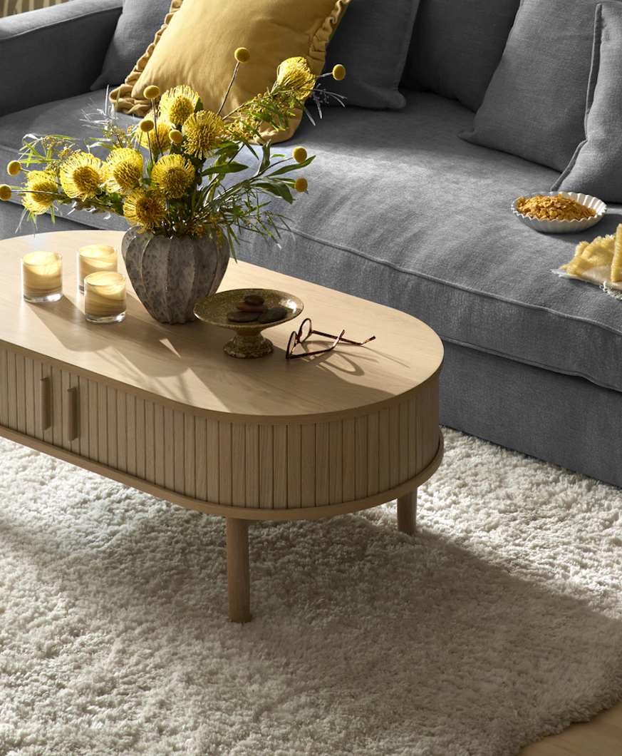 Framför en blå soffa står ett soffbord i vitbetsat trä